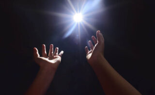 Two hands reaching to the light in darkness: Persecution leads to hope